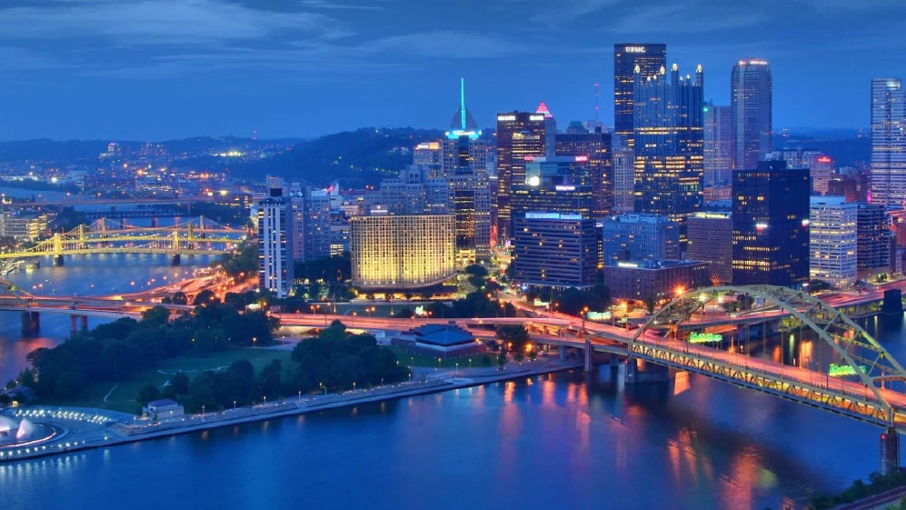 An aerial view of cityscape Pittsburgh surrounded by buildings and water in evening