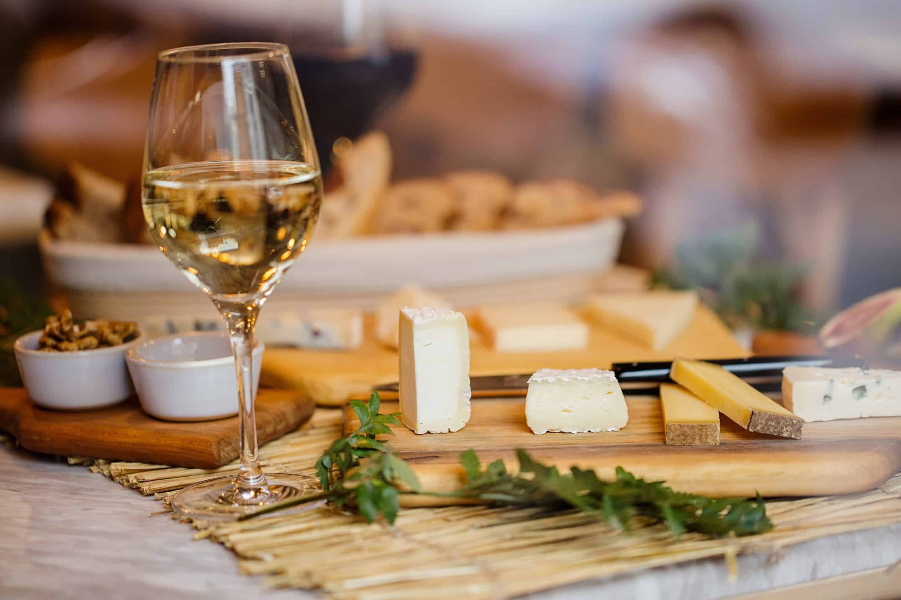Cheese platter arranged with assorted cheeses, and nuts, set on a wooden board in a wine-tasting room.